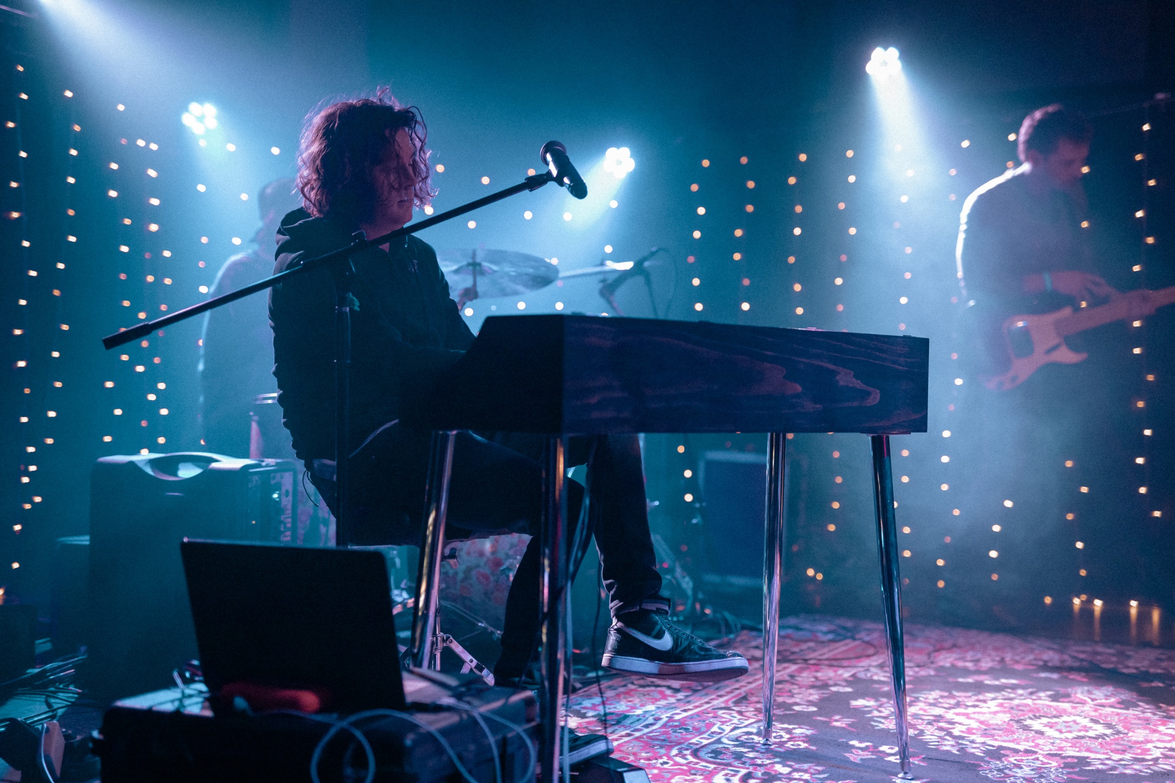 A performer on stage playing a keyboard set inside a handcrafted Piano Shell Company MINI Shell, framed by warm string lights.